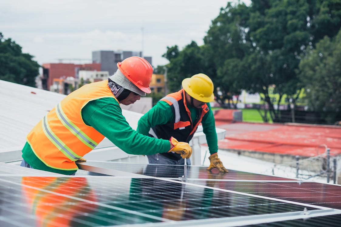 dois profissionais de capacete e colete refletivo instalando e conversando sobre as vantagens da energia solar