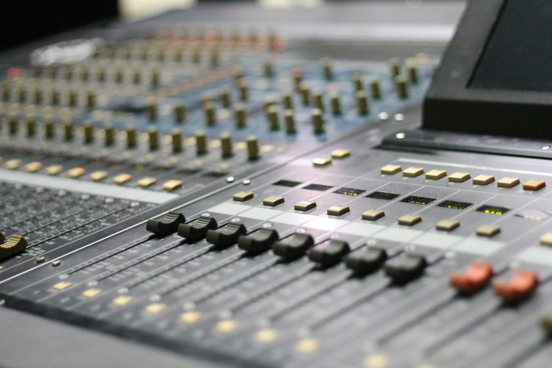 Close-up view of an audio mixer panel with control knobs and sliders in a studio setting.