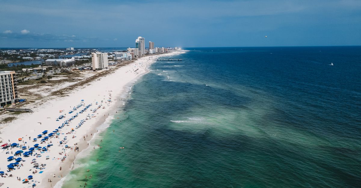 Aerial shot of a bustling beachfront with green waters and tall buildings under a clear sky.