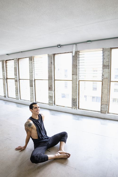 Free Tattooed man sitting on the floor, smiling in a well-lit studio with large windows. Stock Photo