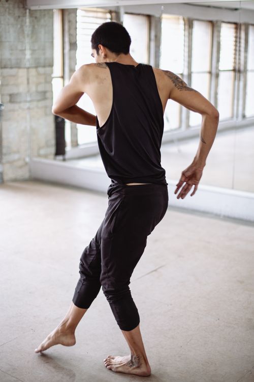 Free A man in a black tank top dancing barefoot in a bright indoor studio with mirrors. Stock Photo