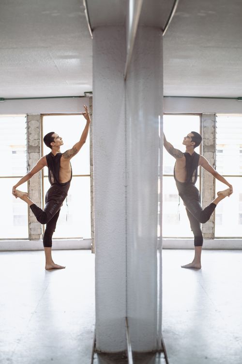 Free Ballet dancer practicing pose in front of mirror in bright dance studio. Stock Photo