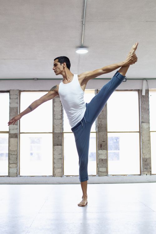 Free A male dancer in white tank top gracefully stretching in a bright indoor studio. Stock Photo
