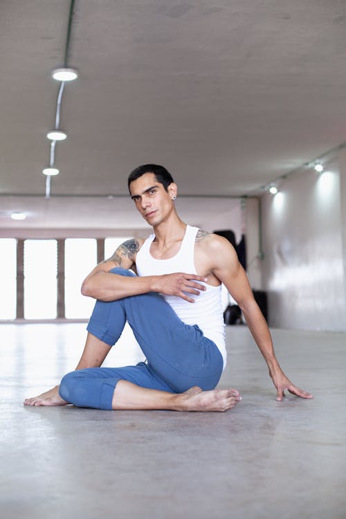 Man in a White Tank Top and Blue Jogging Pants Sitting on a Floor