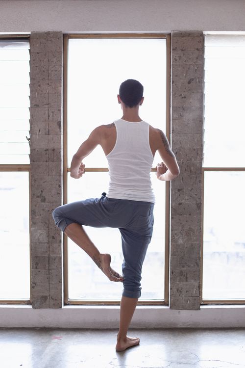Free A man in a yoga pose stands by a window, creating a serene indoor scene. Stock Photo
