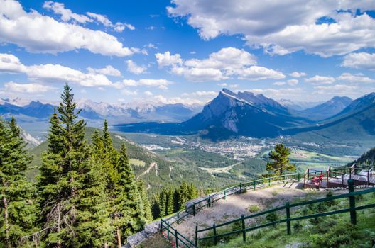 Scenic view from a railing overlooking mountains and a valley under a blue sky with clouds.