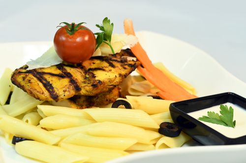 Free Deliciously grilled chicken served on pasta with tomato and olives in a creamy sauce. Stock Photo
