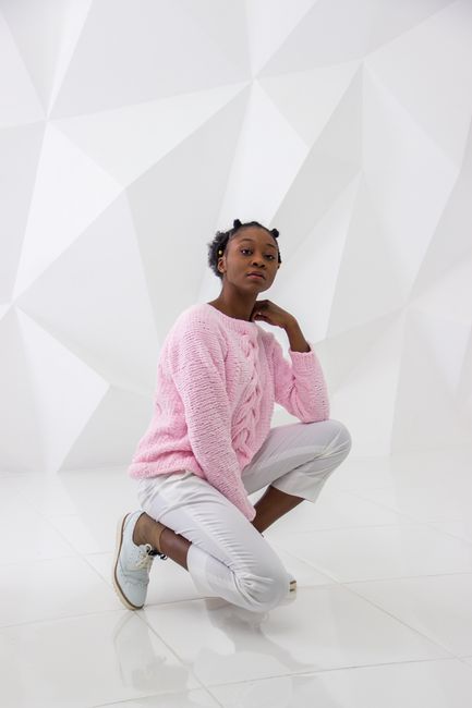 African American woman posing confidently in pink knitwear against a geometric white backdrop.