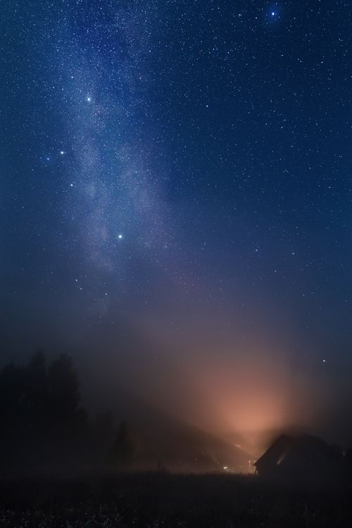 Free A serene view of a starry night sky over a foggy house, showcasing the beauty of constellations and mist. Stock Photo