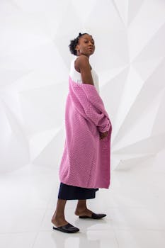 一位优雅的女人身着粉色针织衫，在现代白色背景下摆出姿势