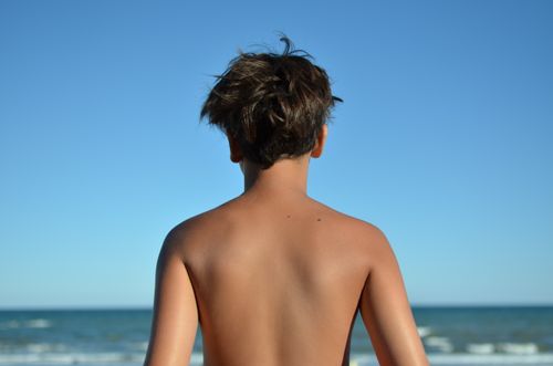 Free A child gazes at the ocean with a clear blue sky above. Stock Photo
