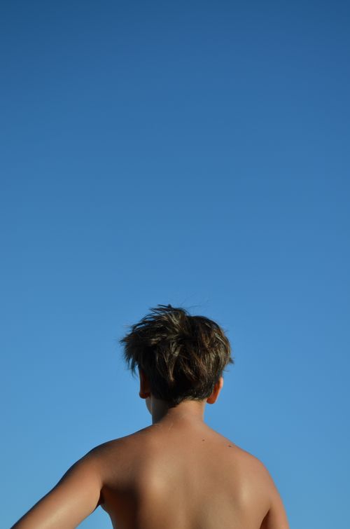 Free Boy gazes at clear blue sky, low angle shot emphasizes serene moment. Stock Photo