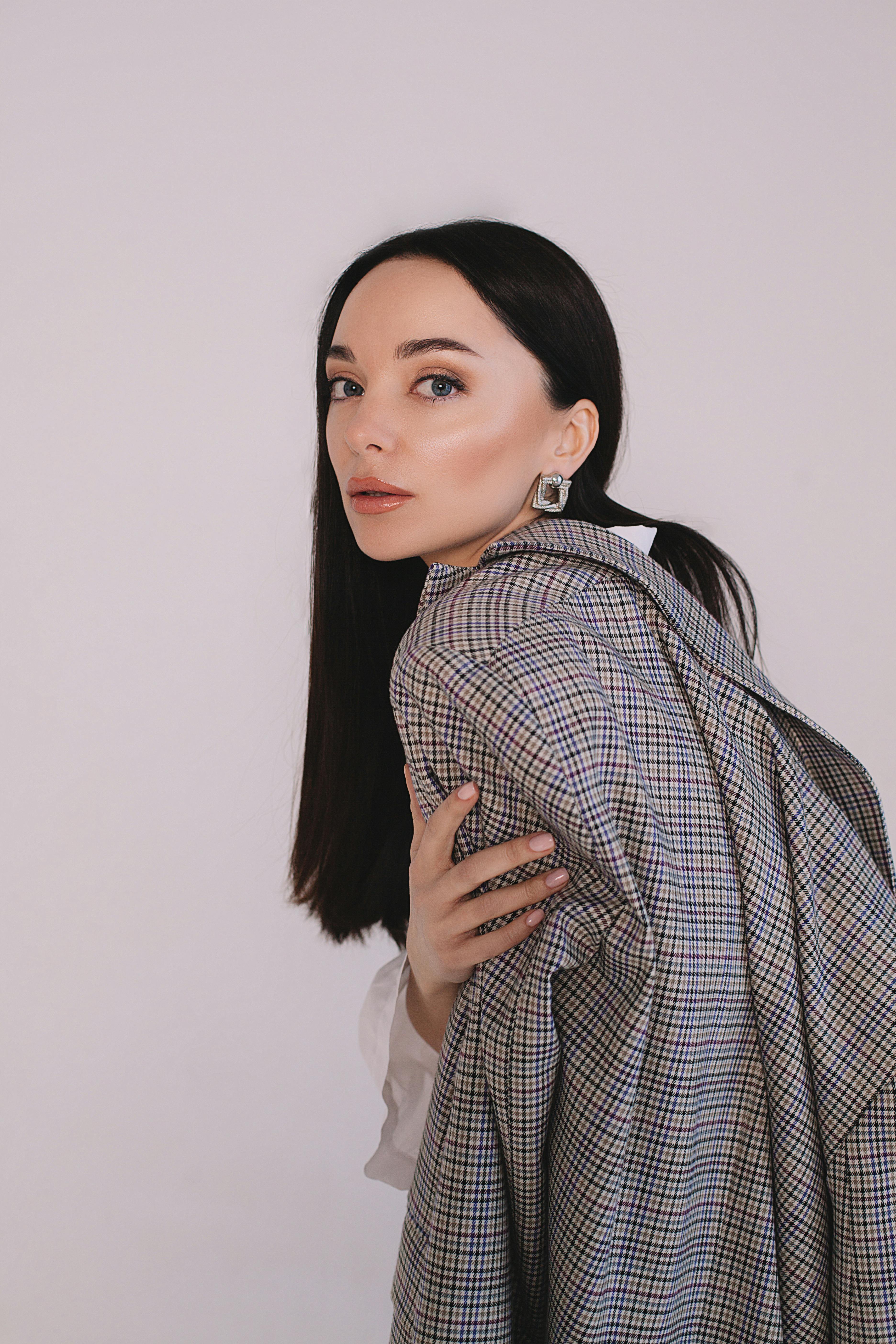 Stylish young woman posing in a plaid jacket against a neutral background.