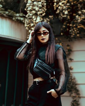 Fashionable adult woman in black outfit and sunglasses posing stylishly outdoors.