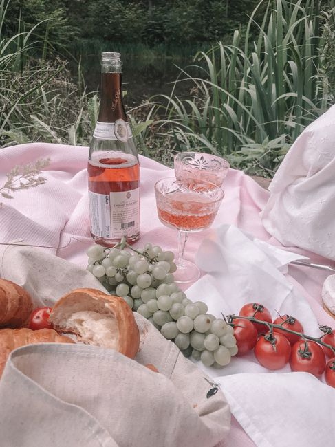 Charming picnic setup with wine, croissants, and fresh fruits in a lush garden setting.