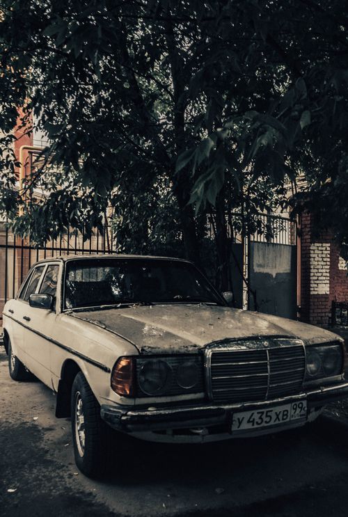 Free A classic vintage car parked under a tree on an urban street, evoking nostalgia. Stock Photo