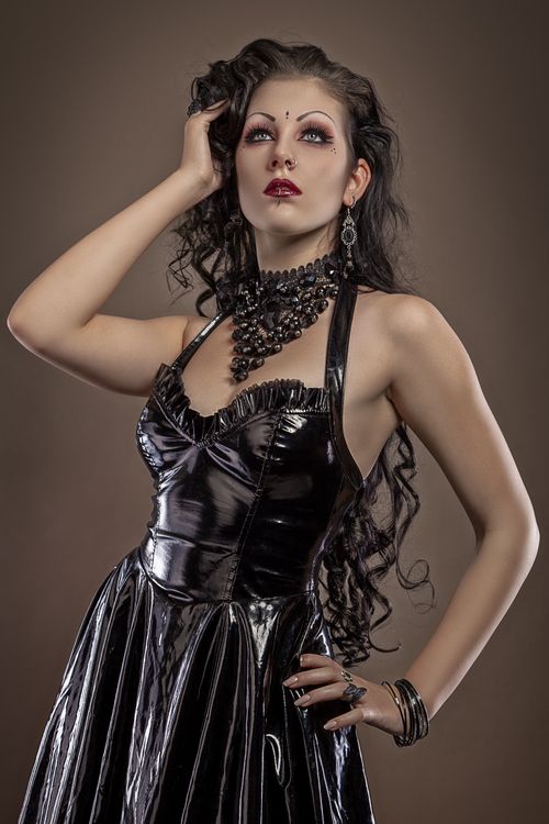 Free Stylish woman in black leather dress with accessories posing against a gray backdrop. Stock Photo