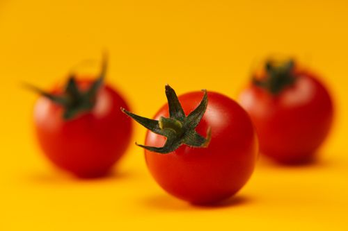Free A vibrant close-up of fresh cherry tomatoes against a bright yellow backdrop, emphasizing healthy food. Stock Photo