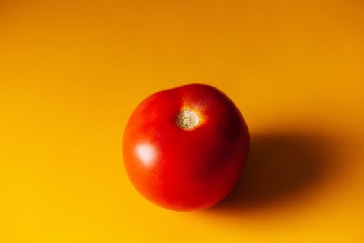 Single red tomato on a bright yellow background, showcasing freshness and vibrant colors.