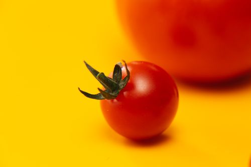 Free A striking close-up of a fresh cherry tomato on a bright yellow background, emphasizing color contrast. Stock Photo