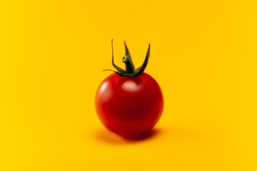 Free Close-up of a fresh cherry tomato on a bright yellow backdrop Stock Photo