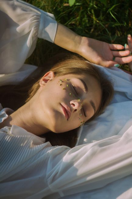 Young woman sleeping on grass in a white dress, conveying tranquility and nature connection.