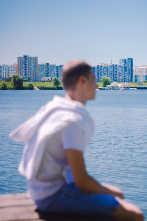 Cityscape Behind a Man Sitting on a Pier