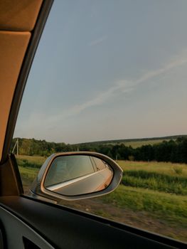 Serene view through a car window of a lush green meadow with clear skies.