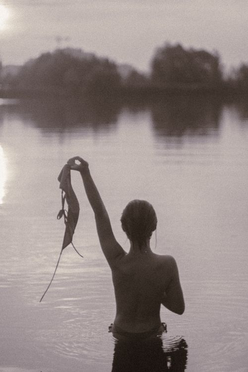 Free Silhouette of a person standing in a lake, holding clothes during twilight. Stock Photo