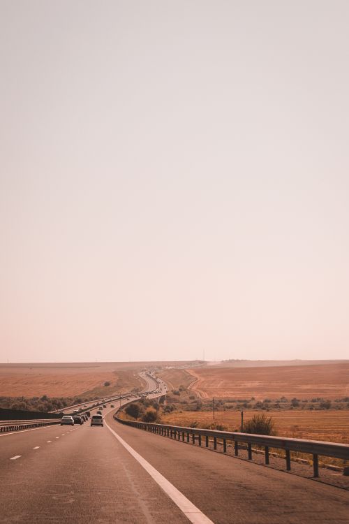Free A picturesque view of an open road stretching through vast fields under a clear sky. Stock Photo