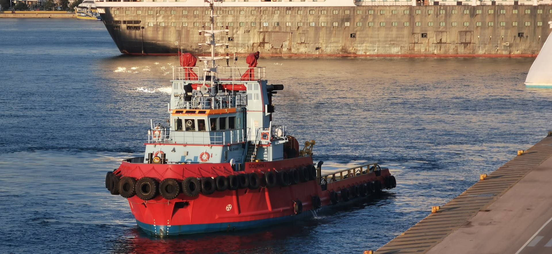 Tugboat in Athens Harbor assisting cargo ships in golden light. Maritime industry scene.