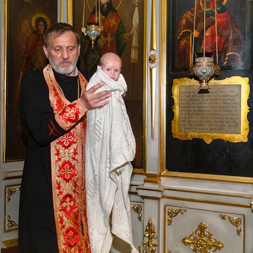 Priest Carrying Child Covered in White Blanket