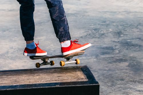 Free Skateboarding action shot with skater performing a trick wearing red sneakers in an outdoor skate park. Stock Photo