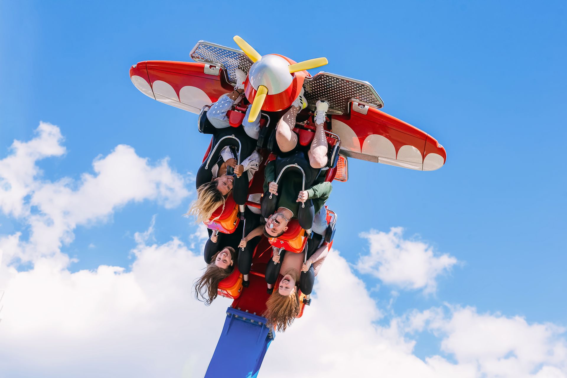Group of friends enjoying an upside-down amusement park ride against a bright blue sky.