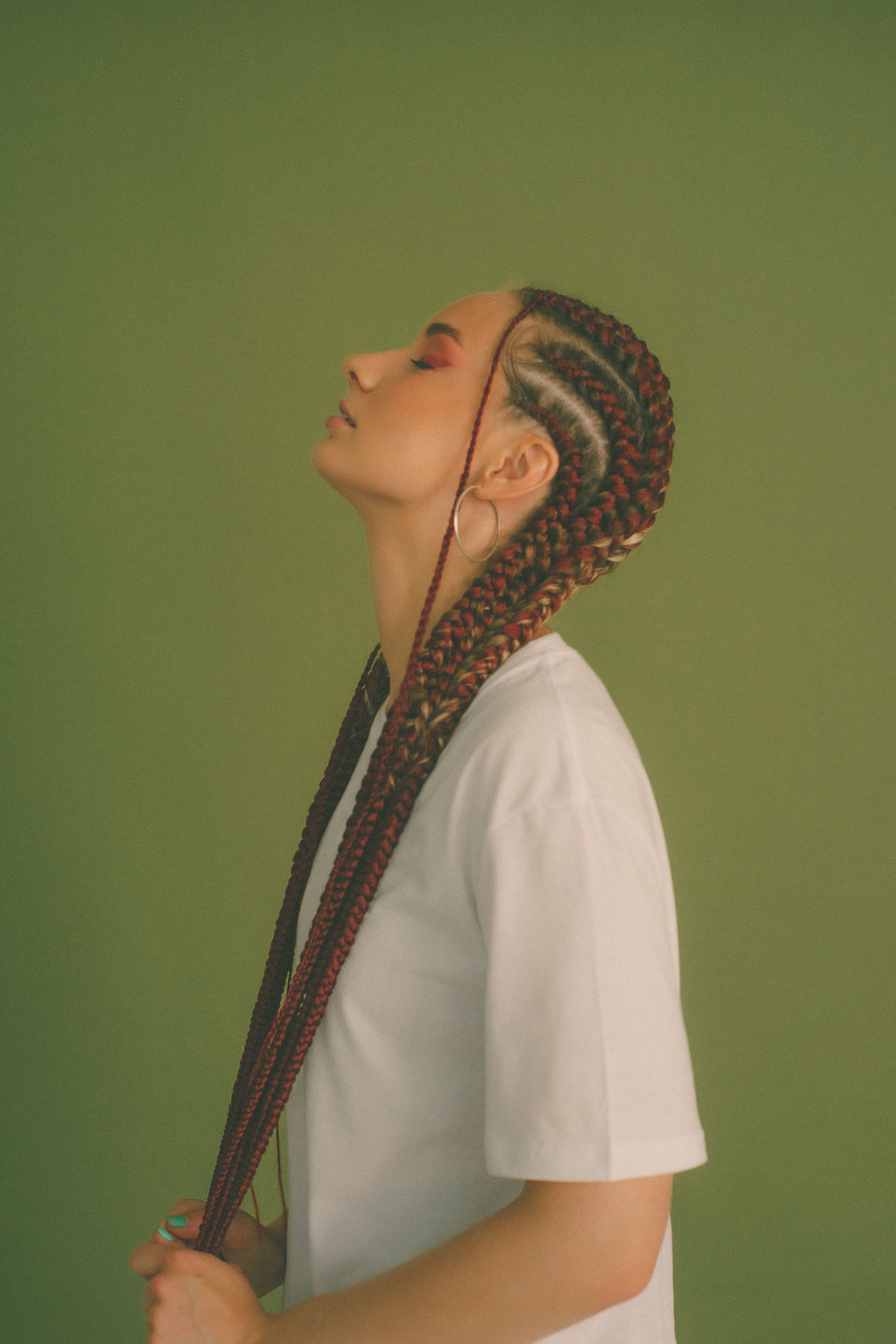 Stylish woman with braided hair and closed eyes against a green backdrop in a studio setting.