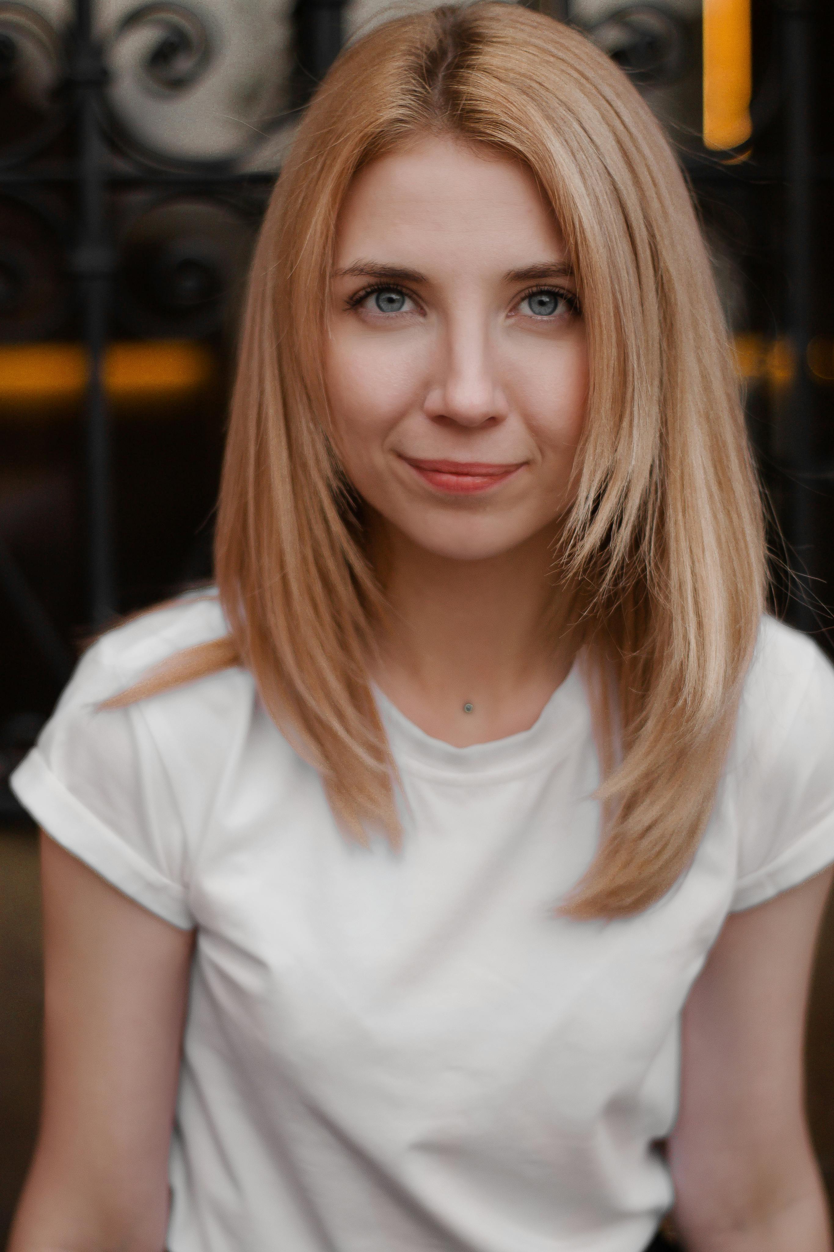 Close-up portrait of a smiling blonde woman in a white top with a soft expression.