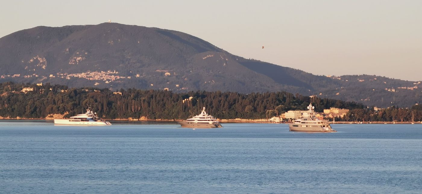 Yachts at anchor off a green coastline at golden hour