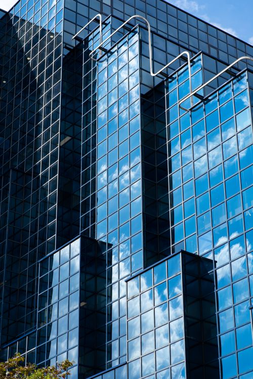 Free A sleek glass facade of a London skyscraper reflecting the bright blue sky and clouds. Stock Photo