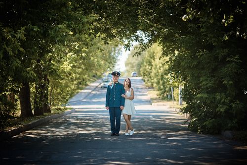 Free A couple standing together on a sunny tree-lined road, embracing under a natural arch of trees. Stock Photo