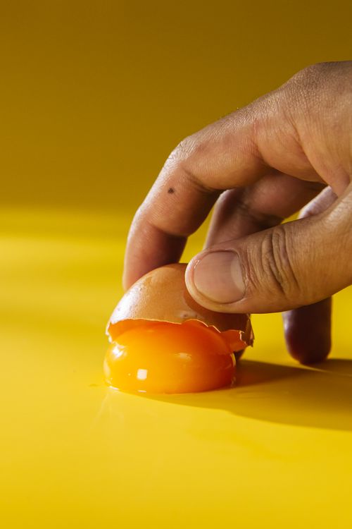 Free A detailed view of a hand cracking an egg with a vibrant yellow background. Stock Photo