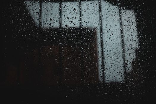 Close-up of raindrops on a window pane with a blurred cityscape. Moody and atmospheric shot.