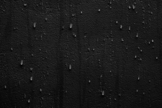 Close-up view of rain droplets on a cracked dark wall creating a moody texture.