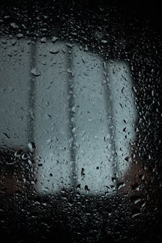 Close-up view of raindrops on window glass creates a moody atmosphere.