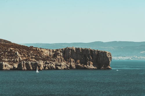 White Boat on Sea Near Brown Rock Formation