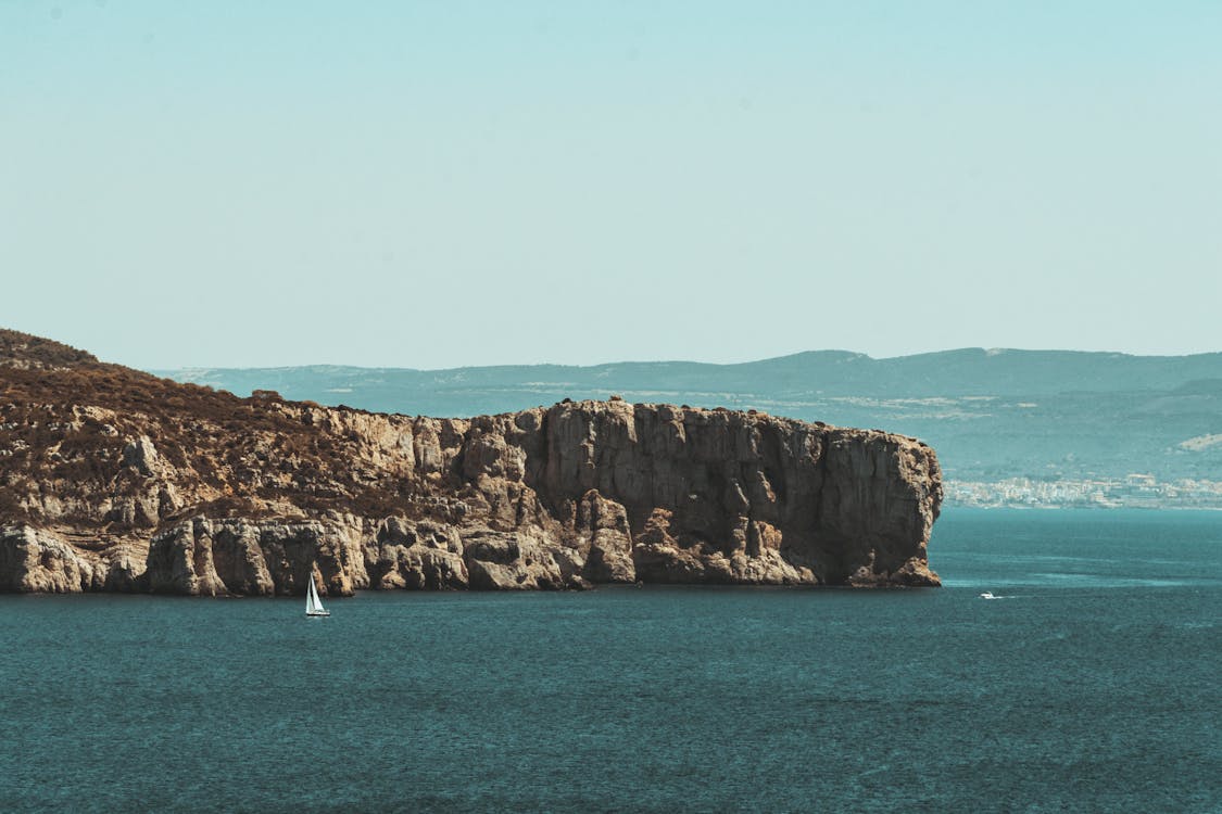 White Boat on Sea Near Brown Rock Formation