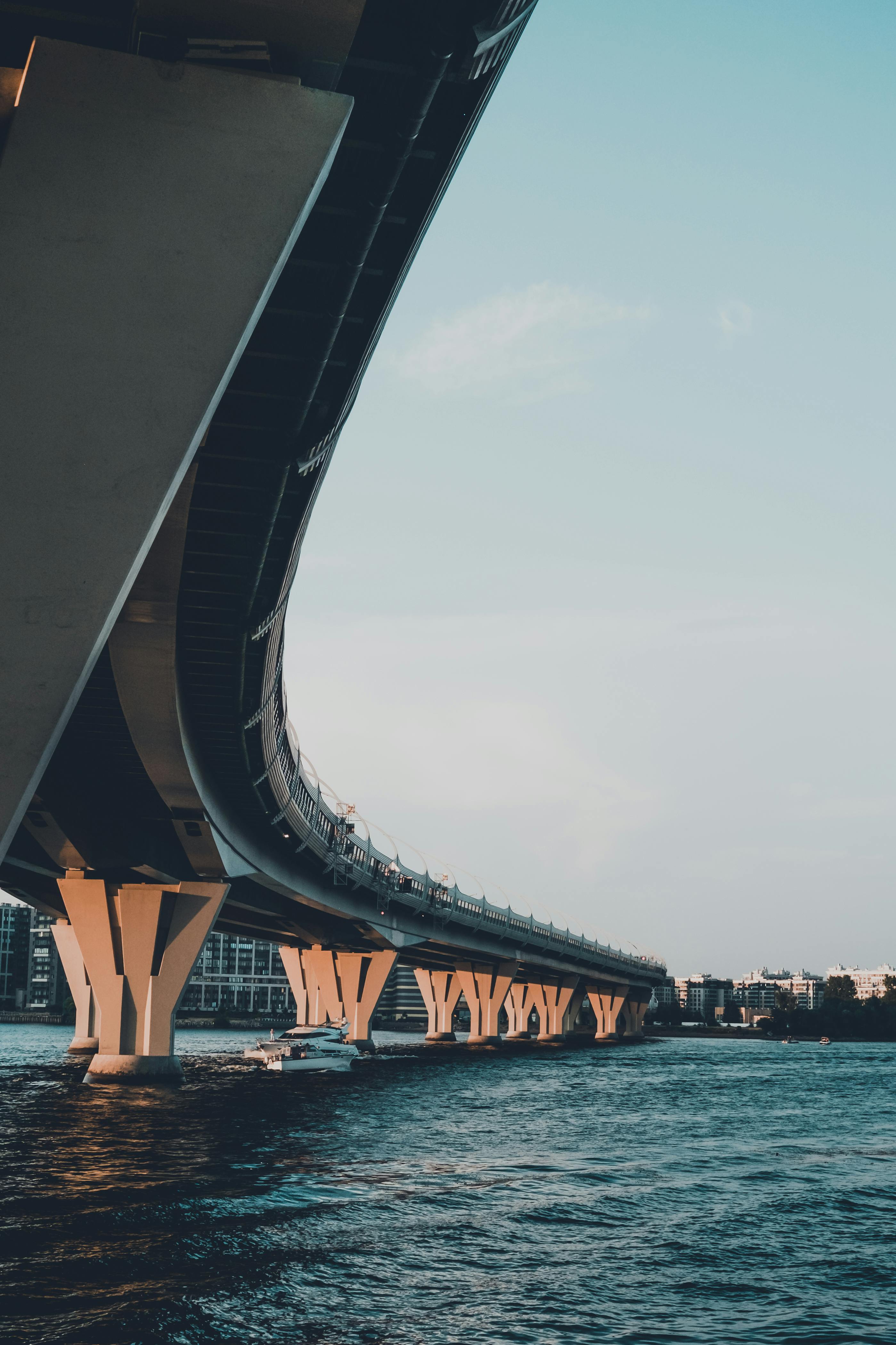 A sleek modern bridge arches over a calm urban waterfront under a clear sky.