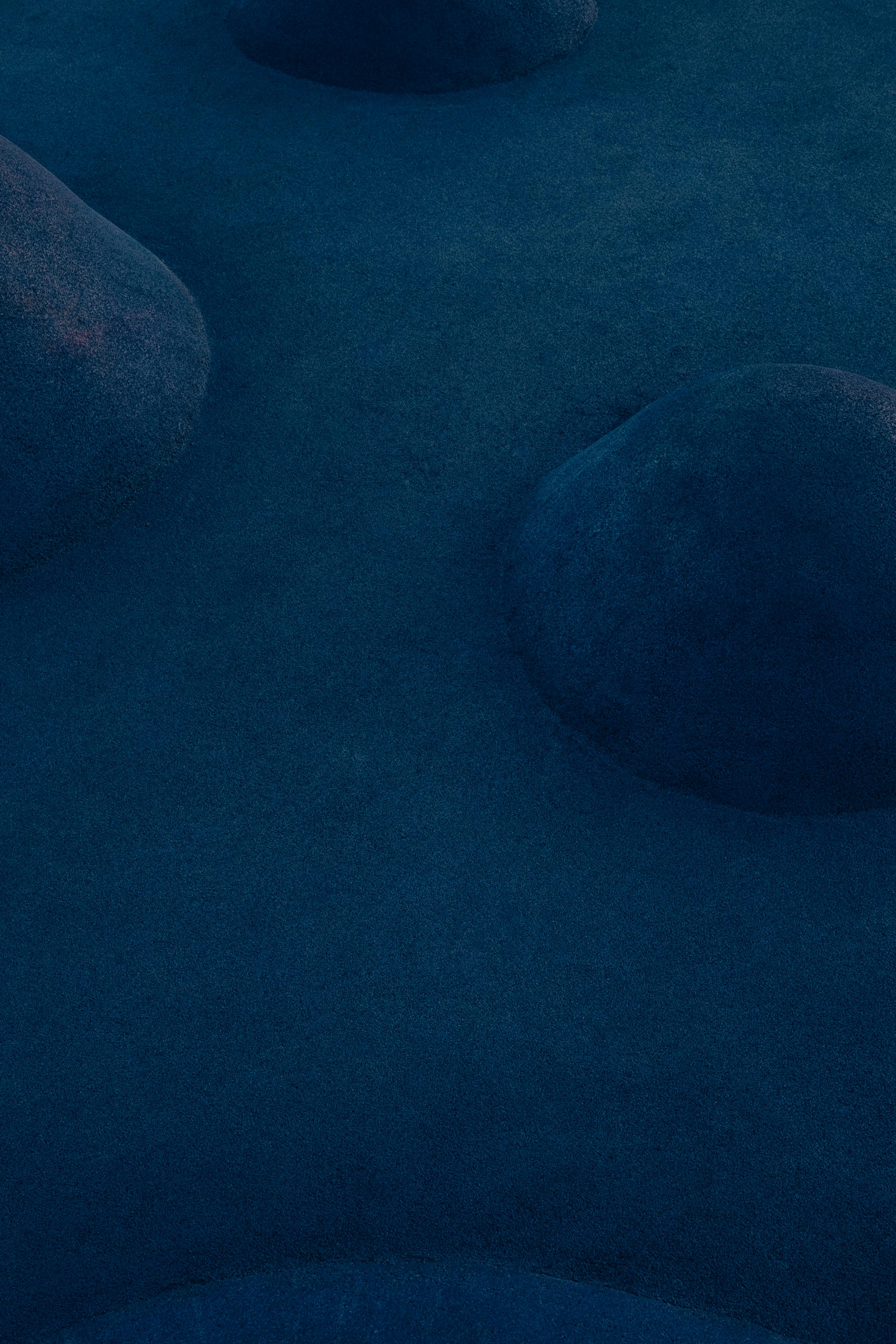 Aerial shot of mysterious blue-lit landscape with smooth ridges and shadows.