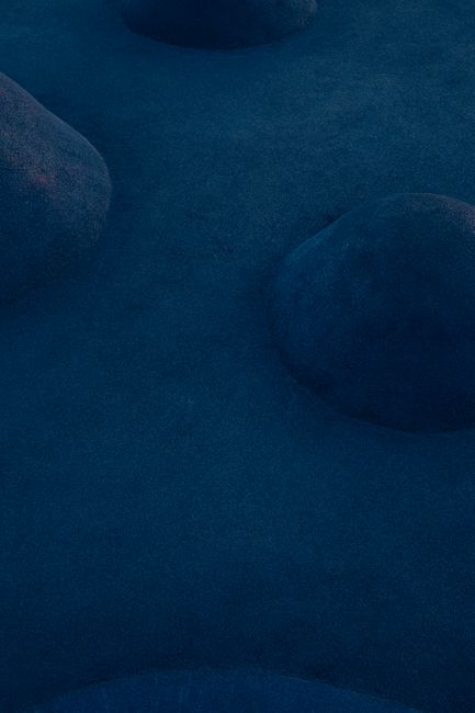 Aerial shot of mysterious blue-lit landscape with smooth ridges and shadows.