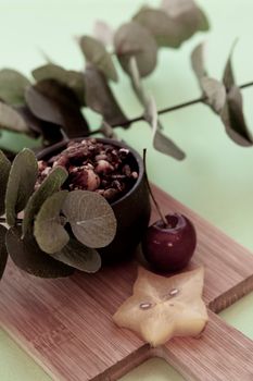 Aesthetic display of starfruit and cherry on a wooden board with eucalyptus leaves.