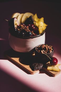 Elegant display of assorted fruits with granola and nuts on a cutting board, lit dramatically.